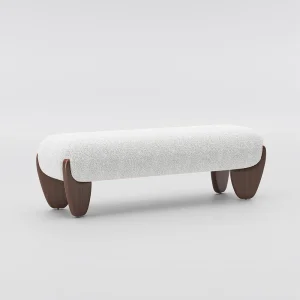 Minimalist bench with white textured cushion and curved wooden legs, placed in a sunlit room with vertical blinds and a tall potted plant.