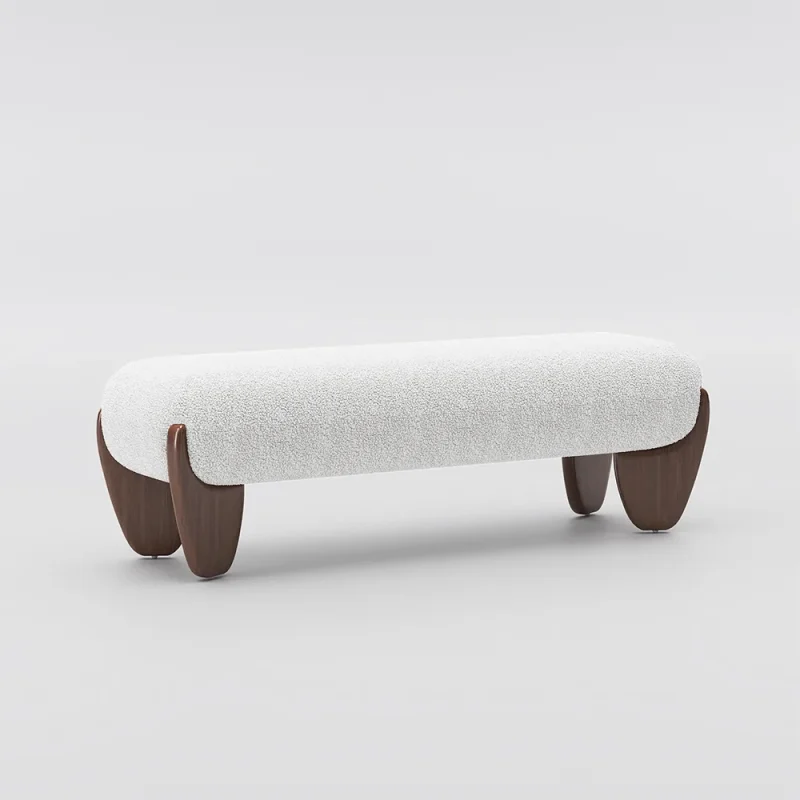 Minimalist bench with white textured cushion and curved wooden legs, placed in a sunlit room with vertical blinds and a tall potted plant.