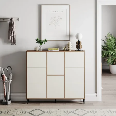 White and wood-toned mid-century modern shoe cabinet with nine compartments, styled with decorative items on top including a lamp, books, and a potted plant; set in a minimalist entryway with coat rack, umbrella stand, and framed botanical artwork.