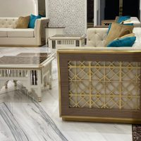 A luxurious lounge ensemble blending geometric craftsmanship, plush symmetry, and layered architectural elegance. Cream tufted sofas with teal cushions, white carved coffee tables, gold lattice panels, and marble flooring.