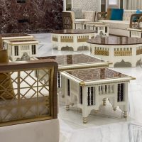 A traditional lounge ensemble blending geometric craftsmanship, rich material contrast, and cultural architectural elegance. Light sofas with lattice arms, white and dark wood coffee tables, marble flooring, and patterned wall panels.