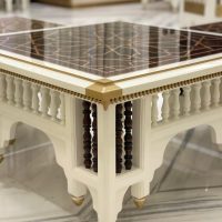 A sculptural accent table blending traditional craftsmanship, bold geometry, and luxurious material contrast. Square table with glossy geometric top, white carved frame, gold trim, and dark spindle legs on marble floor.