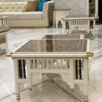 A refined living room vignette showcasing artisanal table design, plush seating, and layered marble textures. White carved coffee table with glossy geometric top, cream tufted sofa with turquoise cushion, marble flooring.