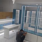 Sleek cabinetry and ambient lighting elevate this retail setup into a refined product showcase. Retail display space with white and blue built-in cabinet, glass shelves, LED lighting, marble flooring, and abstract wall panel in a modern interior.