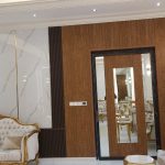 Classical elegance meets modern refinement in this richly detailed living space. Luxurious living room with white and gold tufted furniture, marble and wood wall panels, chandelier lighting, and mirrored door in a classical interior.