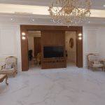 Ornate details and symmetrical elegance define this opulent living space inspired by classical design. Classical living room with white marble flooring, gold-accented chandelier, tufted armchairs, mirrored wall panels, and a central entertainment unit in a luxurious interior.