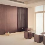 Natural light and clean lines define this airy space, where texture meets simplicity. Minimalist interior with vertical slatted wood accent wall, glass-topped wooden tables, large windows, and recessed ceiling lighting.