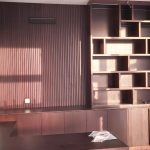 A custom blend of texture and function defines this sleek wall unit, perfect for modern living or workspace design. Built-in wooden wall unit with vertical slatted panel, open shelving compartments, and lower cabinets in a modern interior with natural lighting.