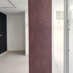 A single wood panel adds warmth and balance to this clean-lined architectural corner. Minimalist interior with vertical wood panel between white wall and glass window, light flooring, and recessed ceiling lighting in a modern space.