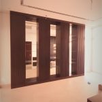 Reflective glass and rich wood textures bring depth and sophistication to this contemporary wall installation. Interior space with built-in dark wood wall unit featuring vertical panels and glass sections, light flooring, and recessed ceiling lighting in a modern setting.