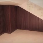 A clever blend of glass and wood transforms this under-stair space into a functional design feature. Staircase with glass railing and enclosed under-stair wall made of vertical wooden slats, set in a modern tiled interior.