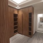 Clean lines and warm wood textures define this elegant dressing space with built-in storage. Walk-in closet with vertical wood grain cabinetry, open shelving, recessed ceiling lighting, and gray-toned flooring in a modern minimalist interior.
