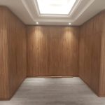 Vertical wood panels and soft lighting bring warmth and structure to this sleek built-in wardrobe design. Interior space with full-wall wooden wardrobe, natural wood grain finish, recessed ceiling lighting, and light gray flooring in a modern minimalist design.