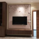 Cherry blossom motifs and natural wood textures bring warmth and elegance to this serene media wall design. Living room wall with cherry blossom mural, wall-mounted TV, wooden console, integrated shelving, and recessed lighting in a modern interior.