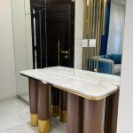 A luxurious console vignette blending reflective surfaces, sculptural lighting, and rich material contrast. Console table with white marble top, mirrored wall, gold partition, and marble flooring in modern interior.