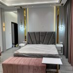 A refined palette of grey, white, and blush pink brings softness and sophistication to this contemporary bedroom. Elegant bedroom with grey geometric headboard, pink bench, white nightstands, and gold-accented lighting in a modern interior.