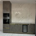 A sleek culinary space blending moody tones, metallic highlights, and sculptural lighting. Modern kitchen with dark grey cabinets, gold accents, marble backsplash, built-in appliances, and light wood flooring.