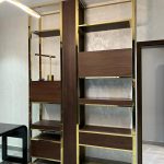 A modern shelving composition blending metallic structure, rich wood tones, and curated display geometry. Built-in shelving unit with gold metal frame, dark wood panels, open compartments, and decorative items.