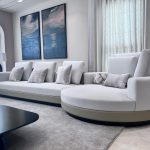 Sculptural seating and soft hues create a serene, gallery-inspired living space with modern elegance. Stylish living room with a light gray sectional sofa, abstract wall art, arched windows with sheer curtains, and a black coffee table with ceramic decor.