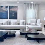 Abstract art and soft textures elevate this minimalist living room, where balance and elegance meet. Minimalist living room with a white sofa, abstract wall art, black coffee tables, and sheer curtains in a neutral-toned modern interior.
