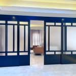 Geometric frosted glass doors add structure and sophistication to this open-plan living space. Black sliding doors with geometric frosted glass panels open to a modern living room with a brown sofa, marble flooring, and warm recessed lighting.