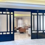 Sleek black-framed sliding doors with frosted glass bring elegance and privacy to this contemporary living room. Black-framed sliding glass doors with geometric frosted panels divide a modern living space featuring a brown sofa, white armchair, and polished tile flooring.