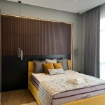 Bold color meets warm textures in this vibrant and contemporary bedroom retreat. Bedroom with yellow upholstered bed, striped rug, pendant lights, wood slat headboard wall, and ambient lighting.