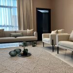 Soft textures and natural light create a serene and sophisticated living space. Living room with beige sofa, matching armchairs, round tray centerpiece, sheer curtains, and neutral decor.