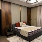 A rich mix of textures and tones brings warmth and elegance to this modern bedroom retreat. Bedroom with grey upholstered bed, rust and beige pillows, geometric headboard wall, and pendant lighting.