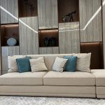 A harmonious blend of textures and tones brings warmth and elegance to this contemporary lounge. Living room with beige sectional sofa, teal and cream pillows, wood-paneled wall, and decorative shelving.