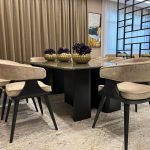 Neutral tones and sculptural accents bring elegance to this contemporary dining arrangement. Dining room with black table, beige upholstered chairs, golden floral centerpieces, and geometric partition.
