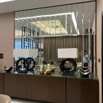 Symmetry and shine define this elegant vignette, where lighting and reflection elevate every detail. Modern interior with segmented mirror wall, wooden sideboard, decorative lamps, and reflective surfaces.